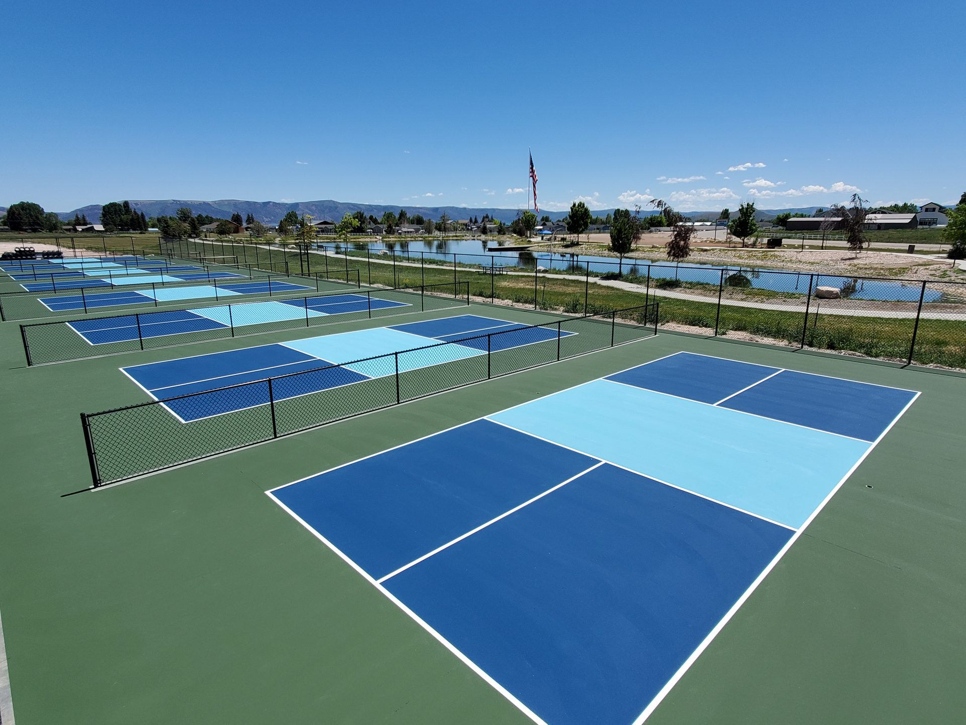 Multi-court pickleball complex with American flag and reservoir view